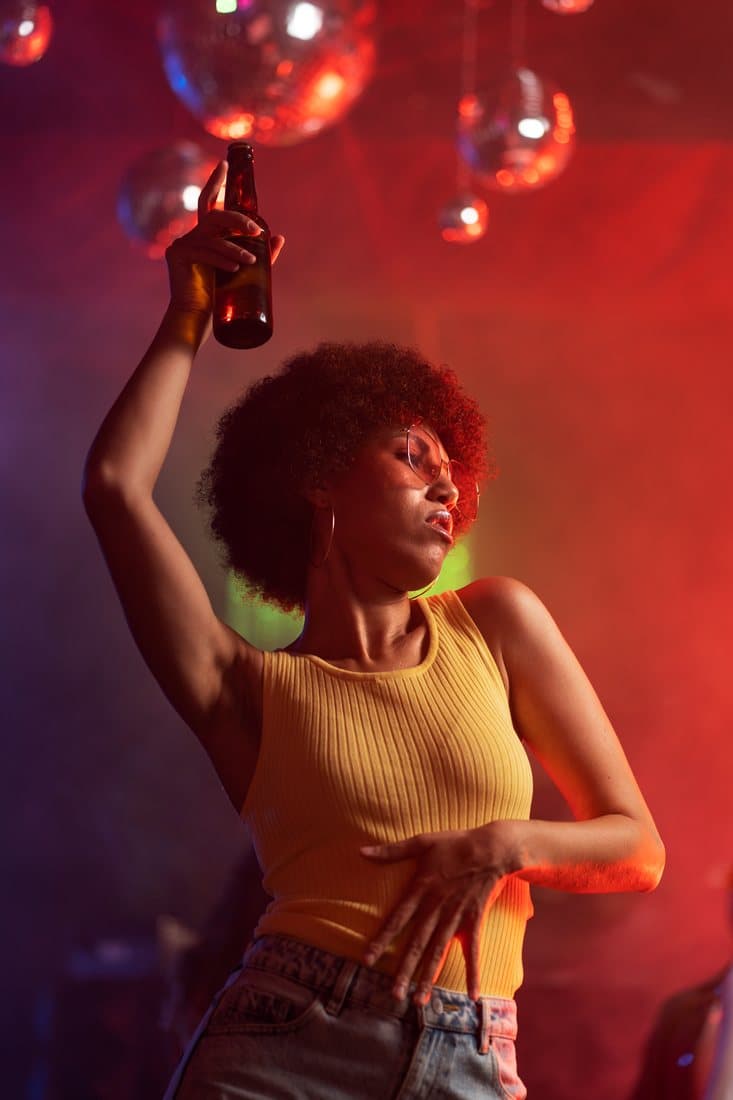 Woman dancing with a bottle raised under disco balls